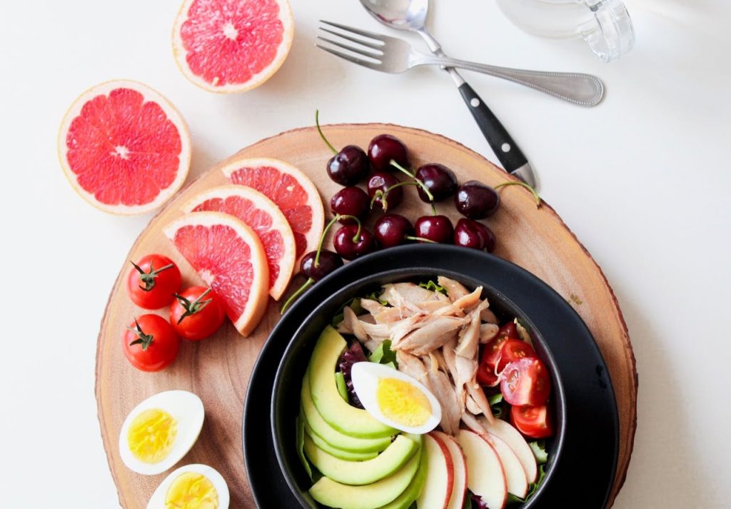 bowl-of-vegetable-salad-and-sliced-fruits-936611 A vibrant breakfast flat lay featuring a mix of fruits, avocado, eggs, tomatoes, and sliced meats on a wooden platter.
